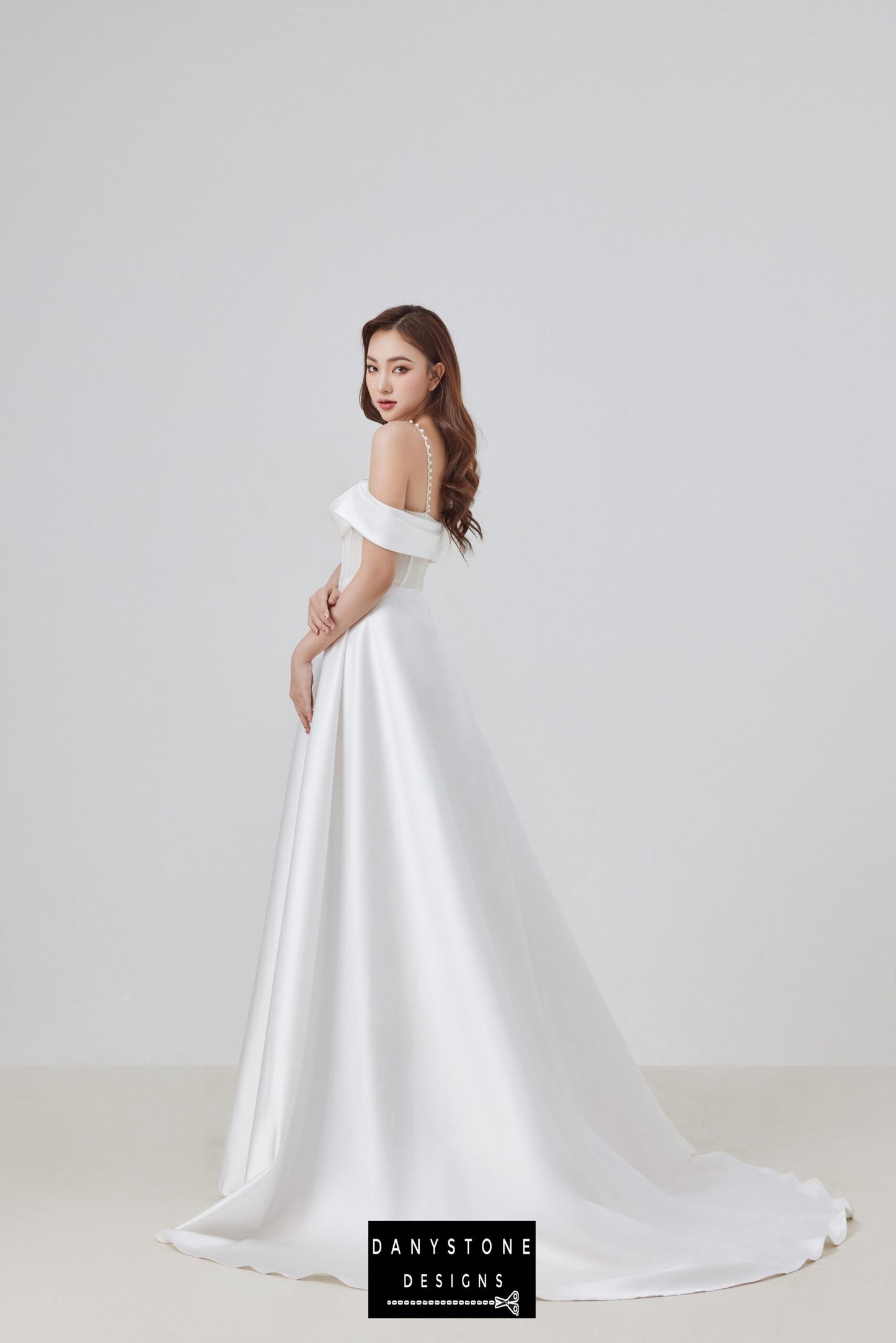 The back view of this elegant satin corset lace off-shoulder wedding dress highlights the delicate pearl straps and the graceful flow of the satin skirt, perfect for a sophisticated bridal look.