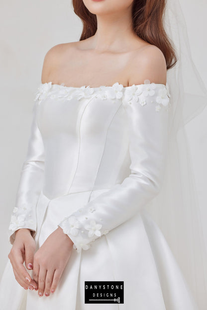 Make a stunning statement on your special day with this elegant off-shoulder taffeta wedding dress, designed for the bride who values sophistication and timeless beauty. Featuring a flat shoulder design, long sleeves, and delicate 3D floral appliqués, this gown is the epitome of modern elegance.