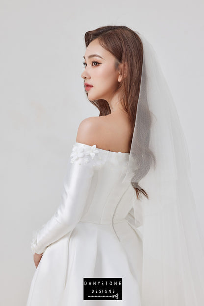 The luxurious off-shoulder taffeta wedding dress with 3D floral appliqués exudes timeless charm and elegance. Designed for the sophisticated bride, this gown highlights a flattering flat shoulder neckline and a structured silhouette.