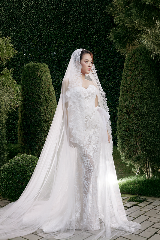 Woman in a white wedding dress with a long veil standing outdoors.