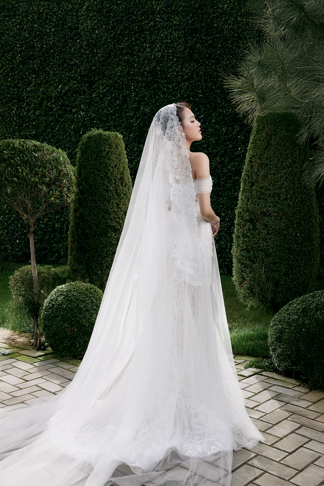 Woman in a white wedding dress with a long veil standing in a garden.