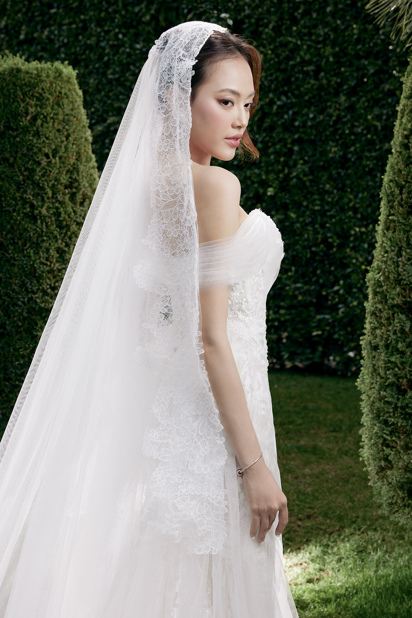 Woman in a white wedding dress with a veil standing outdoors.