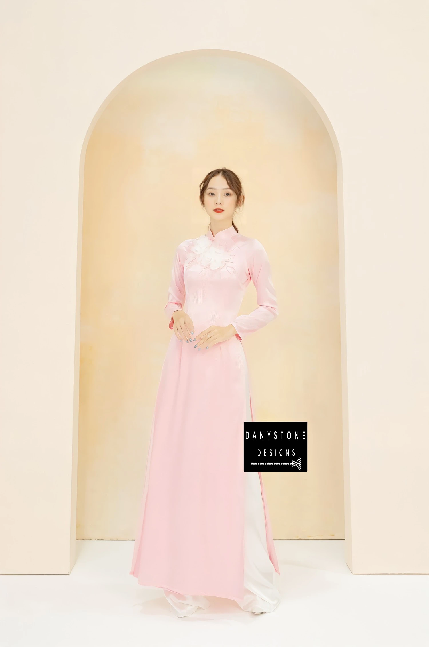 Elegant pink brocade Áo Dài with white chiffon flowers, worn by a bride.