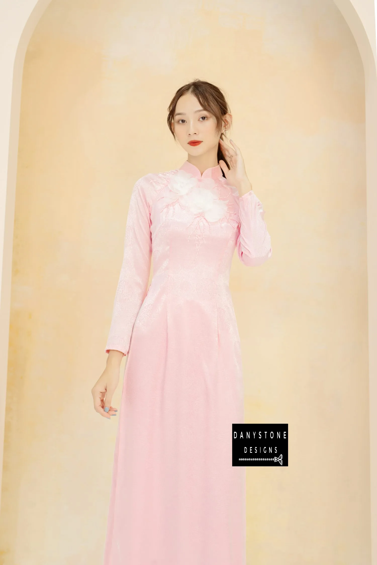 Elegant woman wearing a pink brocade Áo Dài with white floral details.