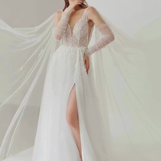 Model wearing a white wedding dress with long sleeves and a slit on a plain background