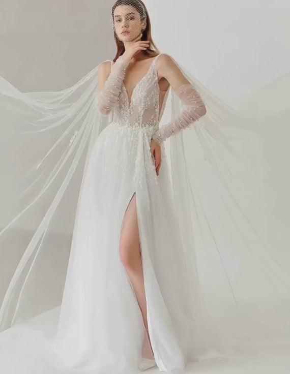 Model wearing a white wedding dress with long sleeves and a slit on a plain background